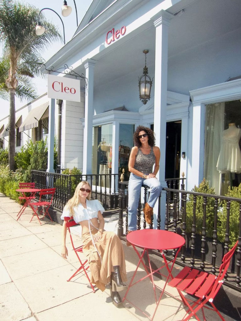 Cleo founders Lexie Jay, seated in a red bistro chair, and Elisabeth Weinstock, sitting on the porch railing, outside the Cleo storefront on West Third Street, Los Angeles